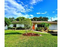Charming single-story home features a well-manicured lawn, tropical landscaping, and a bright orange front door at 2645 Woodring Dr, Clearwater, FL 33759