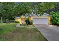 Charming yellow home featuring a white garage door, stone accents, and lush landscaping at 1110 Mercer Loop, Plant City, FL 33567