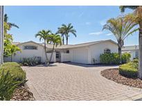 Beautiful single-story home featuring a brick driveway, lush landscaping, and a white exterior at 11225 4Th E St, Treasure Island, FL 33706