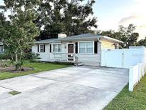 Charming single-story home featuring a well-manicured lawn, private white fence, and long concrete driveway at 114 N Arcturas Ave, Clearwater, FL 33765