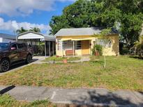 Charming single-story home with yellow siding, covered porch and carport and a mix of grass and weeds in the front yard at 6818 59Th St, N., Pinellas Park, FL 33781