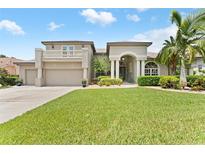 Elegant two-story home featuring lush landscaping, a manicured lawn, and an attached three-car garage at 1553 Canopy Oaks Blvd, Palm Harbor, FL 34683