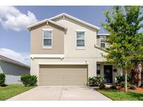 Two-story home featuring a two-car garage, neutral color scheme, manicured lawn, and small shrubs at 17156 Yellow Pine St, Wimauma, FL 33598