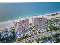 Aerial view of a pink condo building on the beach with tennis courts and well maintained landscaping at 1340 Gulf Blvd # 8C, Clearwater Beach, FL 33767