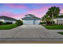 Charming blue two-story home with a two-car garage, lush lawn, and mature palm trees at sunset at 3326 Woodmont Dr, Parrish, FL 34219