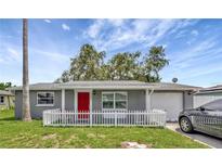 Charming single story home featuring a red door, picket fence, and well manicured lawn at 3426 Coldwell Dr, Holiday, FL 34691
