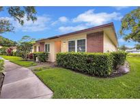 Charming single-story home with manicured lawn, lush greenery, and brick accents at 900 Maclaren N Dr # D, Palm Harbor, FL 34684