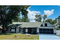 Charming single-story home with a well-manicured lawn, attached garage, and mature trees at 10444 Fordham St, Spring Hill, FL 34608