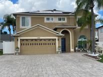 Two-story home with a two-car garage, tan stucco, blue door and a paver driveway framed by palm trees at 1205 Sweet Gum Dr, Brandon, FL 33511