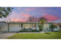 Charming single-story home featuring a white picket fence, attached garage, and freshly manicured lawn under a lovely pink sunset sky at 2025 Jefferson Ave, Dunedin, FL 34698