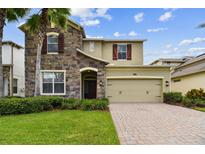 Charming home featuring a stone facade, well-manicured lawn, and a brick paved driveway leading to a two-car garage at 4544 Vermillion Sky Dr, Wesley Chapel, FL 33544