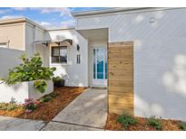 Charming home exterior features a white facade with an awning, modern wood detail, and lush landscaping at 2240 Pinewood Villas Dr, Holiday, FL 34691