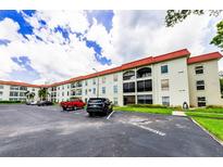 A spacious condo building with a red roof is shown with ample parking in front at 2700 Bayshore Blvd # 1206, Dunedin, FL 34698