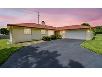 Charming single-story home with a red roof, lush landscaping, and a spacious driveway leading to an attached garage at 855 Pinewood W Ter, Palm Harbor, FL 34683