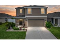 Two-story home featuring a two-car garage, manicured lawn, and charming landscaping at sunset at 636 Olive Conch St, Ruskin, FL 33570