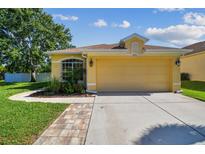 Charming yellow single-Gathering home featuring a well-manicured lawn and attached two-car garage at 11125 Shelter Cove Loop, New Port Richey, FL 34654