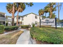 Condominium exterior featuring stucco walls, a sign, palm trees, green shrubs, and a walkway on a sunny day at 4611 W North B St # 228, Tampa, FL 33609