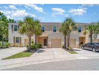 Townhouse exterior featuring a two-car garage, lush palm trees, and neatly landscaped front yard at 12841 Buffalo Run Dr, Gibsonton, FL 33534