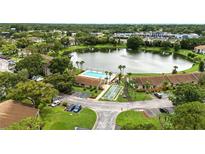 A captivating aerial view showcasing the community pool, serene lake, and lush landscaping at 1725 Pine Ridge E Way # E, Palm Harbor, FL 34684