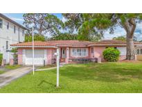 Charming pink home featuring a well-manicured front lawn, a mailbox, and a short driveway leading to an attached garage at 267 Snell Isle Ne Blvd, St Petersburg, FL 33704