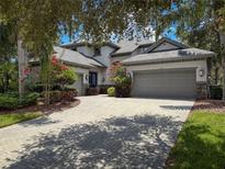 Charming exterior featuring a brick driveway, multi-car garage, and beautiful landscaping with flowering trees at 9808 Milano Dr, Trinity, FL 34655