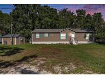 Charming single-story home with brown siding, complemented by lush greenery, a shed and blue window shutters at 2121 Odessa Gardens Ln, Odessa, FL 33556