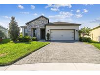 Charming single-story home featuring a stone facade, manicured lawn, and a paved driveway leading to a two-car garage at 6211 Sea Air Dr, Apollo Beach, FL 33572
