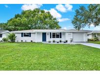Charming home featuring a manicured lawn, fresh paint, and stylish blue accents against a bright sunny sky at 7835 Wallaba Ln, New Port Richey, FL 34653