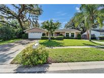 Charming single-story home with a well-manicured lawn, mature trees, and an attached two-car garage at 9403 Bellhaven St, Temple Terrace, FL 33637