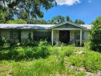 Exterior view of a single-story home with a covered entrance, overgrown lawn, and mature trees at 8109 Franklin Rd, Plant City, FL 33565