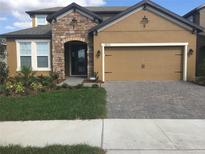 Charming home exterior featuring a stone archway, tan siding, a neat lawn, and a brick driveway at 11613 Sweet Tangerine Ln, Tampa, FL 33626