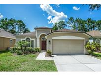 Inviting single-story home with a two-car garage, arched entryway, manicured lawn, and lush green landscaping at 11837 Derbyshire Dr, Tampa, FL 33626