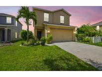 Charming two-story home featuring a well-manicured lawn, palm tree, and two-car garage at sunset at 1012 Seminole Sky Dr, Ruskin, FL 33570