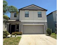 Two-story home featuring a gray exterior, a two-car garage, and a well-manicured lawn with mature landscaping at 10221 Carloway Hills Dr, Wimauma, FL 33598