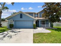 Beautiful blue home with a lush green lawn, complemented by decorative stone accents and fresh landscaping at 1032 Jacob Way, Odessa, FL 33556