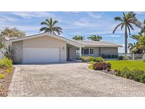 Charming single-story home with a brick driveway, lush landscaping, and a two-car garage at 11055 7Th E St, Treasure Island, FL 33706