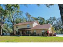 Two-story home with tan siding, brick accents, mature trees, and a well-manicured lawn create curb appeal at 11414 Donneymoor Dr, Riverview, FL 33569
