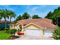 Charming yellow home featuring a tile roof, three-car garage, and lush tropical landscaping with mature palm trees at 1358 Forestedge Blvd, Oldsmar, FL 34677