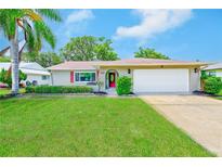 Charming single-story home featuring a lush green lawn, vibrant landscaping, and a bright red front door at 8402 Roxboro Dr, Hudson, FL 34667