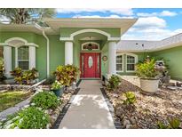 Inviting home entrance with a red door, columns, and decorative landscaping at 1271 Candlelight Blvd, Brooksville, FL 34601