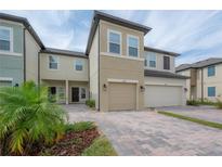 Inviting townhouse with a two-car garage, brick paved driveway, and manicured landscaping at 2469 Stapleford Pl, Wesley Chapel, FL 33543