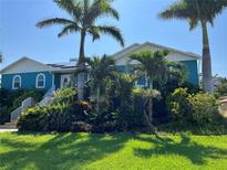 Charming blue house with lush landscaping, mature palm trees and white trim at 803 3Rd S Ave, Tierra Verde, FL 33715
