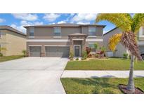 Two-story home featuring a three-car garage, stone accents, and beautifully landscaped front yard at 9456 Channing Hill Dr, Sun City Center, FL 33573