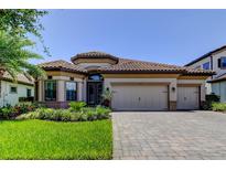 Beautiful single-story home featuring a tile roof, lush landscaping, and a paver driveway leading to a three-car garage at 4372 Night Star Trl, Odessa, FL 33556