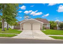 Charming home features a two-car garage, mature landscaping, and a well-maintained lawn on a sunny day at 3226 Cloverplace, Palm Harbor, FL 34684