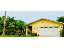 Charming yellow home featuring a two-car garage, lush landscaping, and great curb appeal at 1964 Arvis E Cir, Clearwater, FL 33764