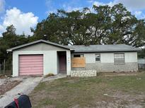 Single-story home with a pink garage door, boarded window, and stone accents on the lower half of the exterior walls at 6804 N 47Th St, Tampa, FL 33610