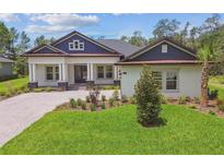 Beautiful home exterior featuring a well-manicured lawn, paver driveway and a welcoming columned porch at 6109 Dusk Rose Ln, Brooksville, FL 34601