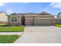 Charming single-story home featuring a red front door, neutral paint, stone accents, and an attached two-car garage at 13822 Bee Tree Ct, Hudson, FL 34669