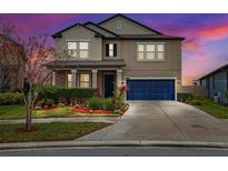 Charming two-story home featuring a well-manicured lawn, vibrant flower beds, and a stylish blue garage door at 9173 Shadyside Ln, Land O Lakes, FL 34637